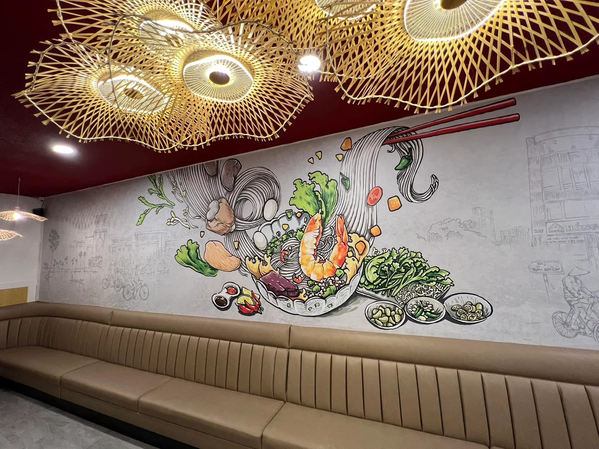 A mural of a bowl of noodles with shrimp and herbs above the booth seating